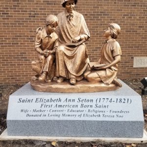 This Bronze Memorial honoring Seton is a custom monument features a large bronze statue with three figures mounted on a grey granite slab with engraving to commemorate the person honored, Saint Elizabeth Ann Seton. Located in Cincinnati, Ohio.