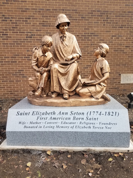 This Bronze Memorial honoring Seton is a custom monument features a large bronze statue with three figures mounted on a grey granite slab with engraving to commemorate the person honored, Saint Elizabeth Ann Seton. Located in Cincinnati, Ohio.