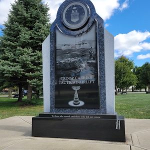 The Tactical Airlift Memorial is crafted from gray and polished blue granite. It is in an upright configuration featuring laser engraved images and memorial information. The memorial is topped with the Seal of the United States Air Force. It is on display at the National Museum of the United States Air Force in Dayton, Ohio.
