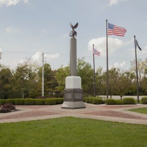 The Beavercreek Veterans Memorial Park is crafted from white, gray, and black granite. It is formed using a black granite pedestal with memorial information engraved on all four sides. There is a white plinth that supports a gray column projecting into the air. A sculpture of an eagle perched on a globe serves as the top of this memorial.