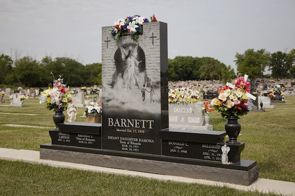 This Custom Companion Bench Memorial honoring Barnett is crafted from Asian Black granite and is comprised of a  upright tablet flanked by twin benches and flower urns. The benches have dedications and the central upright has a laser engraved image of people being welcomed into heaven. It is located in Byron Cemetery, Fairborn, Ohio. The memorial is suitable for use with cremation or traditional interment.