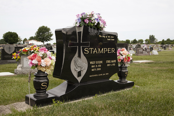 This Custom Companion Upright with Custom Vases monument, rendered in black granite, is irregular in shape, features twin flower urns, and engraved cross intertwined with hands in prayer. The vases are large and each is engraved with a gilded letter S. This memorial is suitable for use with cremation or traditional interment.