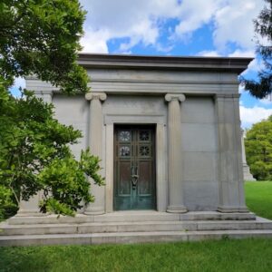 The Historic Carew Mausoleum is crafted from White Victoria Granite in the style of a Greek temple with columns. It features an ornate bronze door.