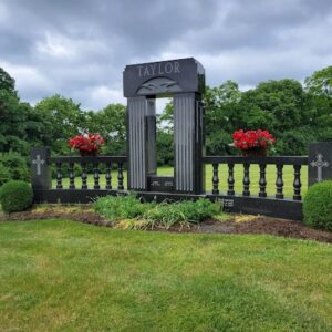The Taylor Family Estate Memorial is crafted from polished back granite and consists of a central arch and two flanking rail components with end cap towers. It features a carving of an eagle on the archway and crosses on each tower. This memorial is appropriate for use with cremation or traditional interment.