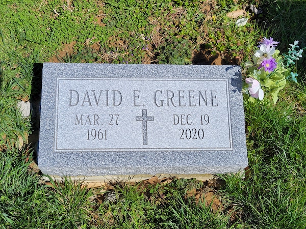 This Single Bevel Marker honoring Greene is crafted from gray granite and features an engraved cross. It is suitable for use with traditional interment or cremation.