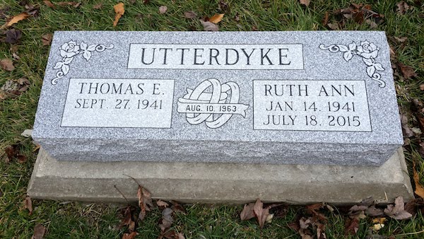 This Companion Bevel Marker honoring Utterdyke is crafted from Rock of Ages gray granite. It features an engraving of intertwined rings and floral accents. This memorial is suitable for traditional interment or cremation.