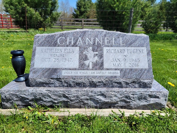 This Companion Slant Memorial honoring Channell is crafted from blue granite and has one flanking vase. It features an engraving of a cross with doves and has an included base. This memorial is suitable for traditional interment or cremation.