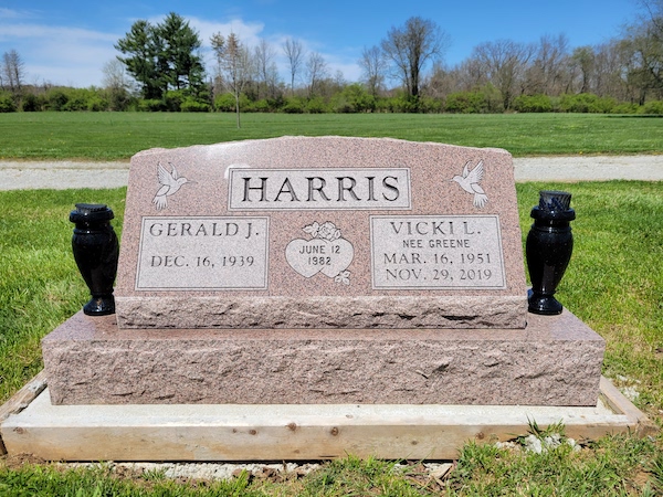This Companion Slant on a Base honoring Harris is crafted from pink granite and is flanked by two vases. It features engravings of doves and joined hearts. This memorial is appropriate for use with cremation or traditional interment.