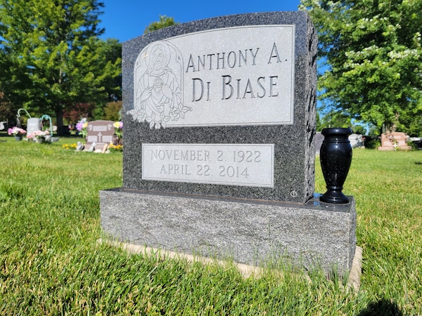 This Single Upright honoring Di Biase is crafted from Rock of Ages blue granite and is flanked by one vase. It features an engraving of the image of Jesus and memorial information. This memorial is suitable for use with cremation or traditional interment.