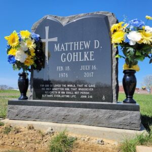 This Custom Single Upright with Rough Edge is crafted from polished and raw black granite. It features an irregular polished shape against a rough finish on the perimeter with an engraved cross and memorial information. This monument is suitable for use with cremation or traditional interment.