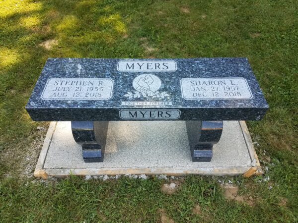 This Companion Bench Memorial crafted from Blue Granite features a carving of doves with a floral accent. This memorial is suitable for use with cremation or traditional interment.