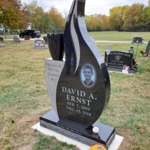 This Custom Single Upright in Flame Shape is crafted from polished black granite. The monument features a single, large vase and a laser engraved image of the decedent. This memorial is suitable for use with cremation or traditional interment.