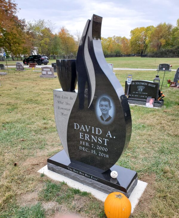 This Custom Single Upright in Flame Shape is crafted from polished black granite. The monument features a single, large vase and a laser engraved image of the decedent. This memorial is suitable for use with cremation or traditional interment.