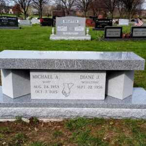 This Companion Custom Bench Memorial was crafted from Rock of Ages gray granite. It features two square columns rotated 90 degrees and an upright between the base and the bench bottom with a carving of joined hands. This memorial is suitable for use with cremation or traditional interment.