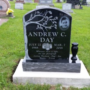 This Single Upright with Laser Engraved Face crafted from polished black granite is flanked with a vase. It features a photo realistic image of the decedent and carvings of a tree and a 35mm camera. This memorial is appropriate for cremation or traditional interment.