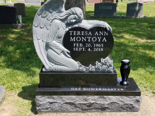 This Custom Single Upright with Vase memorial features a stone shaped in to accommodate the image of a carved angel protecting a heart where the memorial information is presented. The marker, crafted in black polished granite is appropriate for traditional interment or cremation.