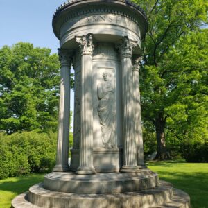 This Estate Monument for the Earnshaw Family is crafted from gray granite and is in a cylindrical shape with Greek columns, a richly carved roof, and cylinder vault with carved figures wearing togas. This estate monument is a 3D work of art and is appropriate for traditional interment or cremation.