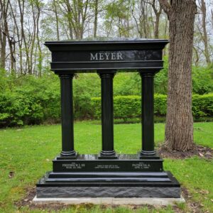 This Custom Companion Upright Greek Column Style is crafted from polished black granite and takes the form of a classic Greek column memorial. It has 3 upright columns and a lentel with the carved with the family name. The base is engraved with the memorial information of the family members. This memorial is suitable for use with cremation or traditional interment.