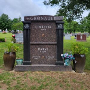 The Gronauer Double Mausoleum is crafted from brown and black granite in an upright configuration. It features columns using the black granite and two plates between them for memorial information. The roof area contains a stylized version of the Gronauer family name. This memorial is appropriate for traditional interment or cremation.
