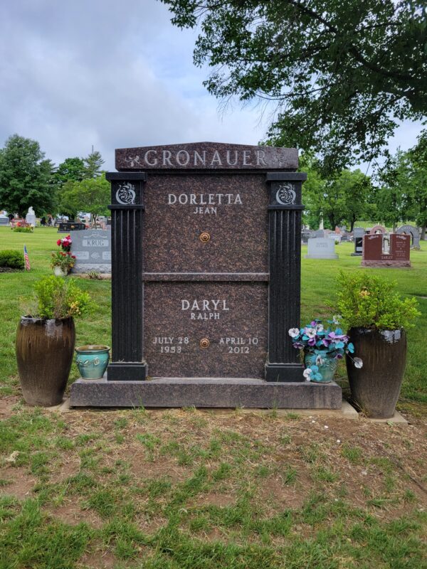 The Gronauer Double Mausoleum is crafted from brown and black granite in an upright configuration. It features columns using the black granite and two plates between them for memorial information. The roof area contains a stylized version of the Gronauer family name. This memorial is appropriate for traditional interment or cremation.