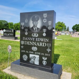 This Single Upright with Laser Engraved Medals is crafted from polished black granite. This memorial features laser engravings including a photo realistic image of the decedent surrounded by military medals representing achievement and recognition of his career. This memorial is suitable for cremation or traditional interment.