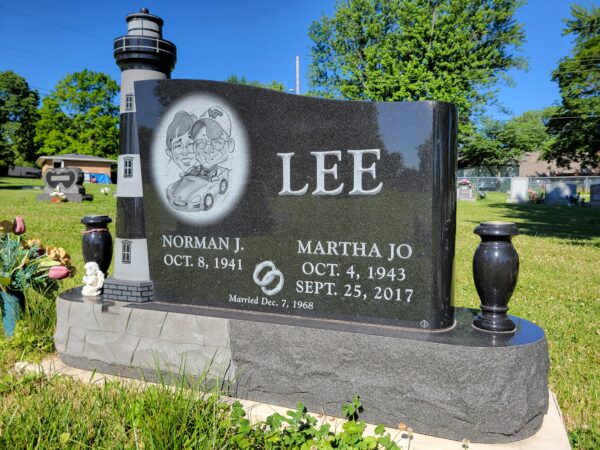 This Custom Companion Upright with Lighthouse is crafted from polished and rough black granite. The memorial features a carved 3-D lighthouse next to the upright and engraved image in cartoon format of the decedents. It is flanked by two large urns. This memorial is suitable for use with cremation or traditional interment.