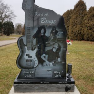 This Custom Single Upright with Laser Engraved Guitar is crafted from polished black granite and is shaped to fit the outline of a guitar. The memorial features laser engravings of a photo realistic guitar and several images of the decedent playing the guitar. This monument is appropriate for use with traditional interment or cremation.