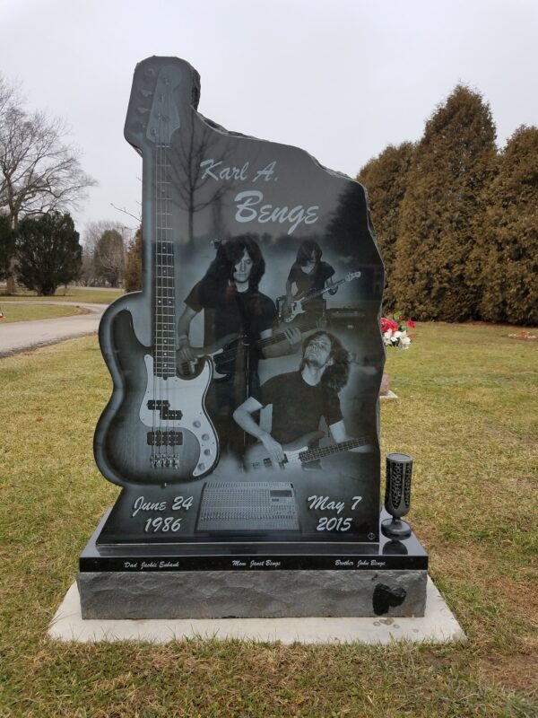 This Custom Single Upright with Laser Engraved Guitar is crafted from polished black granite and is shaped to fit the outline of a guitar. The memorial features laser engravings of a photo realistic guitar and several images of the decedent playing the guitar. This monument is appropriate for use with traditional interment or cremation.