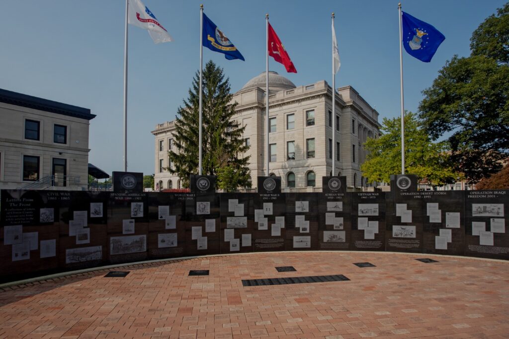 The Clinton County Area Veterans Memorial is crafted from polished black granite in the form of a curved wall with five pedestals each supporting a flag pole. The memorial has a section dedicated to each war/conflict and the area veterans who served in them. The flags on the poles represent the 5 branches of military service in the United States. You can see this memorial in person at the Clinton County courthouse in Wilmington, Ohio.