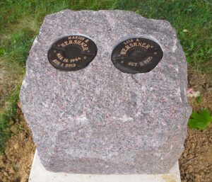 This creative and natural memorial is crafted from a rustic mahogany granite with separate bronze niches for loved one's cremains. While simple, this design integrates well into a natural setting and is striking in its appearance.