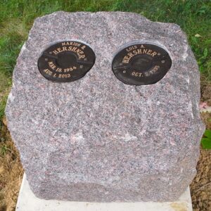 This creative and natural memorial is crafted from a rustic mahogany granite with separate bronze niches for loved one's cremains. While simple, this design integrates well into a natural setting and is striking in its appearance.
